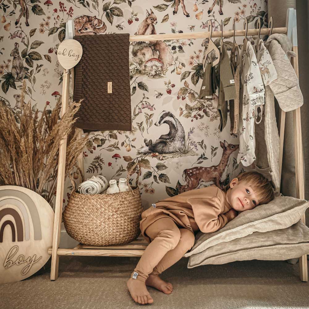 Dekornik Cute Forest Animals Light Behang — Een lief behang met schattige bosdieren — vosjes, eekhoorns en hertjes — tussen bomen, in lichte tinten, perfect voor een warme, natuurlijke kinderkamer. Sfeerbeeld van het behang in een ingerichte kinderkamer.