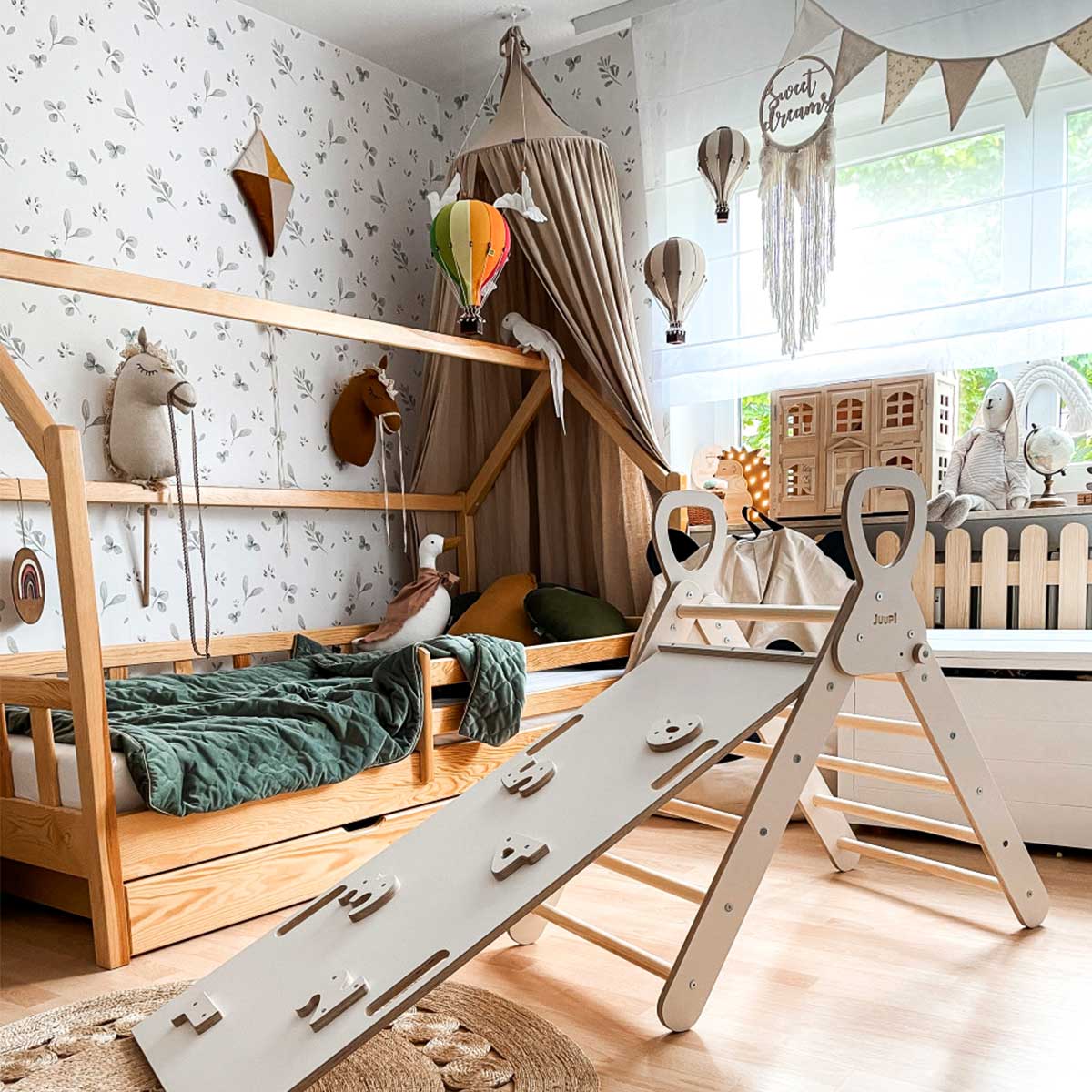 Dekornik Clover Beige/ Return To Innocence Behang — Een rustig behang met kleine klavertjes in beige en zachte groentinten, perfect voor een serene, natuurlijke kinderkamer. Sfeerbeeld van het behang in een ingerichte kinderkamer.