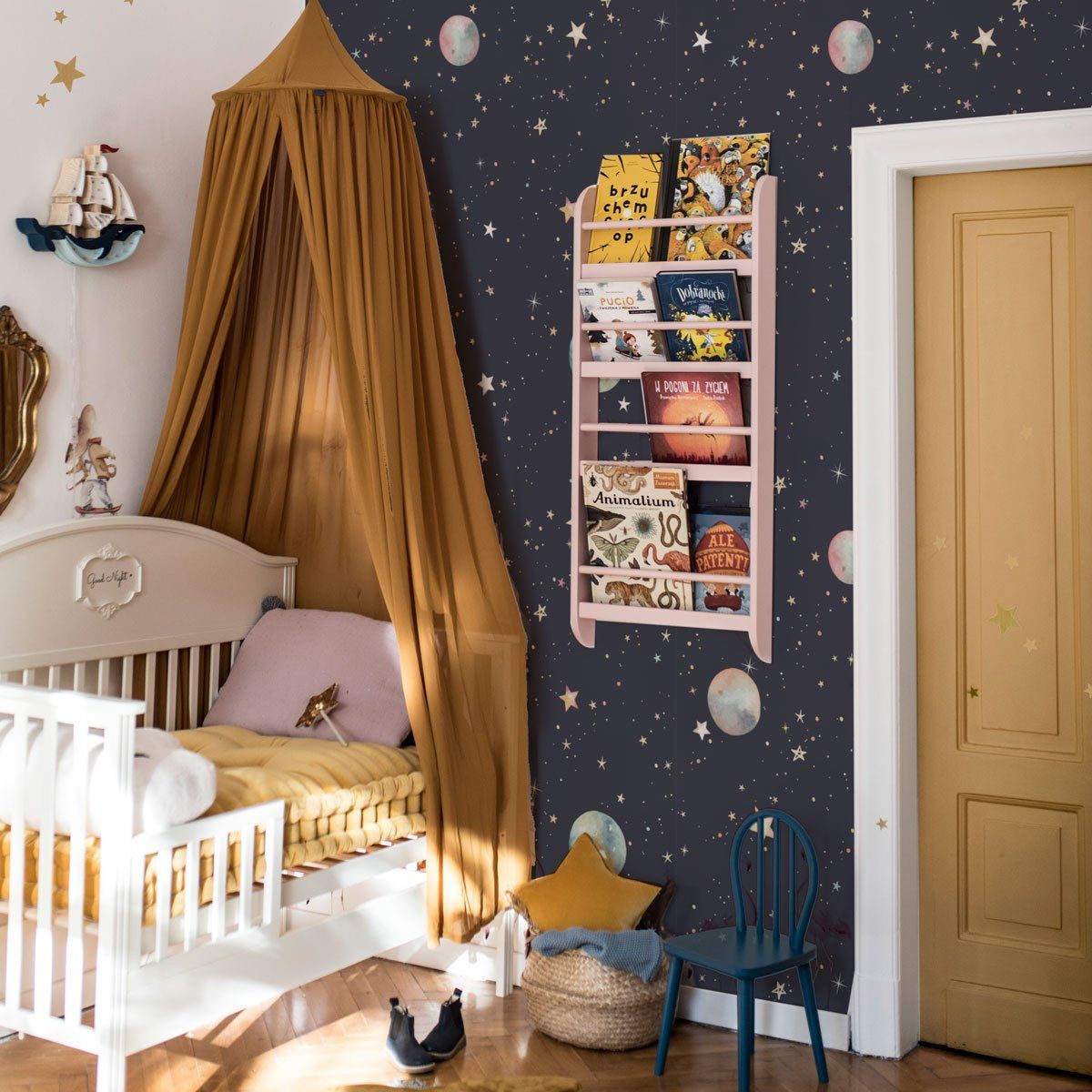 Dekornik Cosmos Behang — Een magisch behang met sterren, planeten en kometen die door een donkerblauwe nachtelijke hemel zweven, perfect voor een dromerige ruimtevaart-kinderkamer. Sfeerbeeld van het behang in een ingerichte kinderkamer.