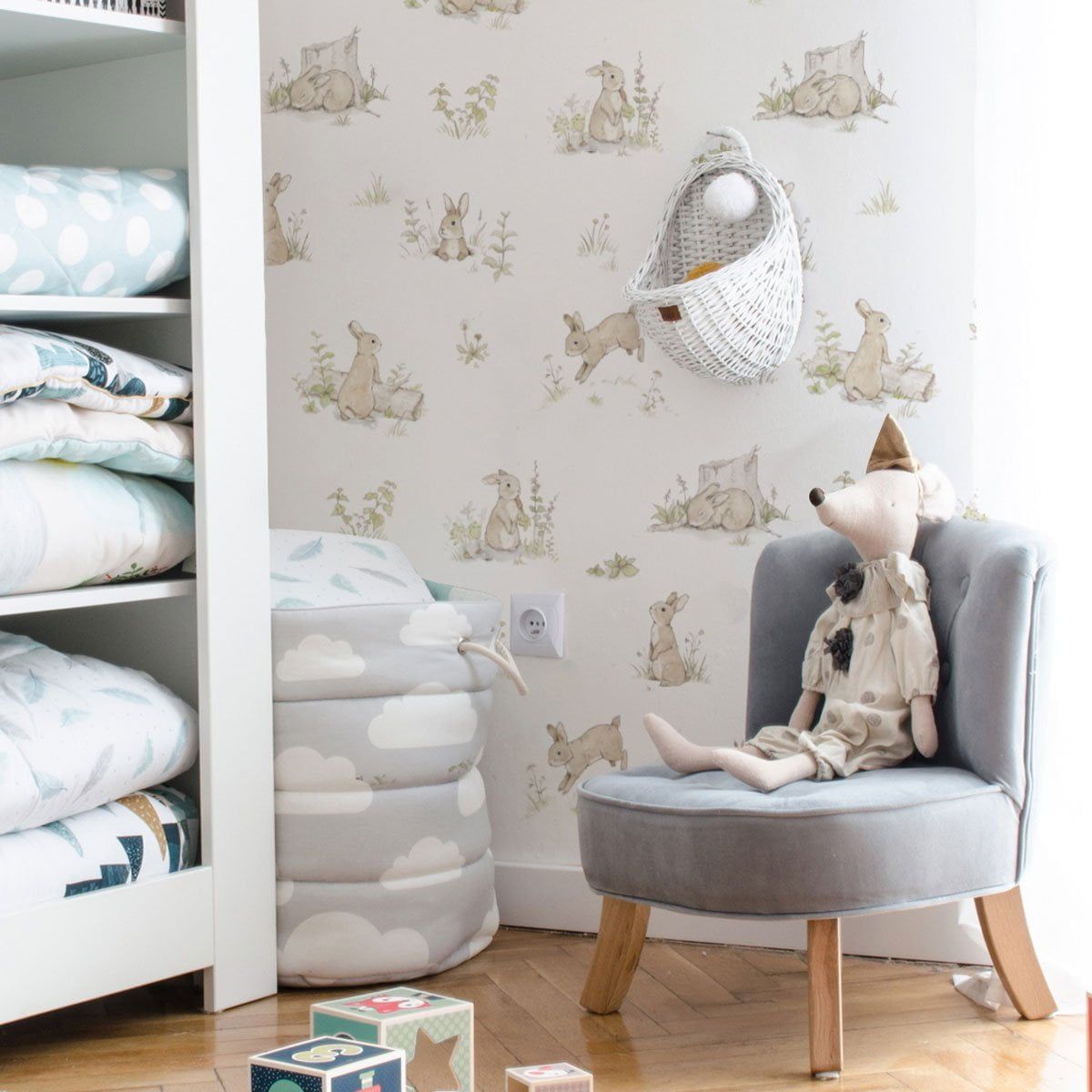 Dekornik Rabbit Day Classic Behang — Een klassiek behang met spelende konijntjes tussen bloemen en gras, in tijdloze kleuren, perfect voor een lieve kinderkamer. Sfeerbeeld van het behang in een ingerichte kinderkamer.