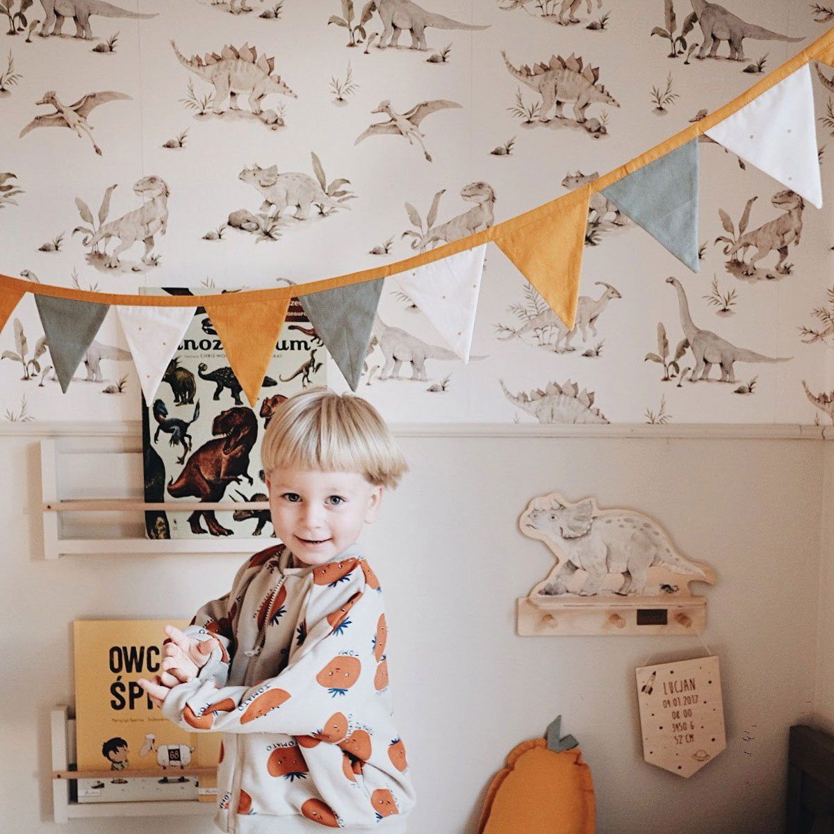 Dekornik Happy Dino's Behang — Een vrolijk behang met speelse dinosaurussen in vriendelijke kleuren, perfect voor een avontuurlijke kinderkamer. Sfeerbeeld van het behang in een ingerichte kinderkamer.
