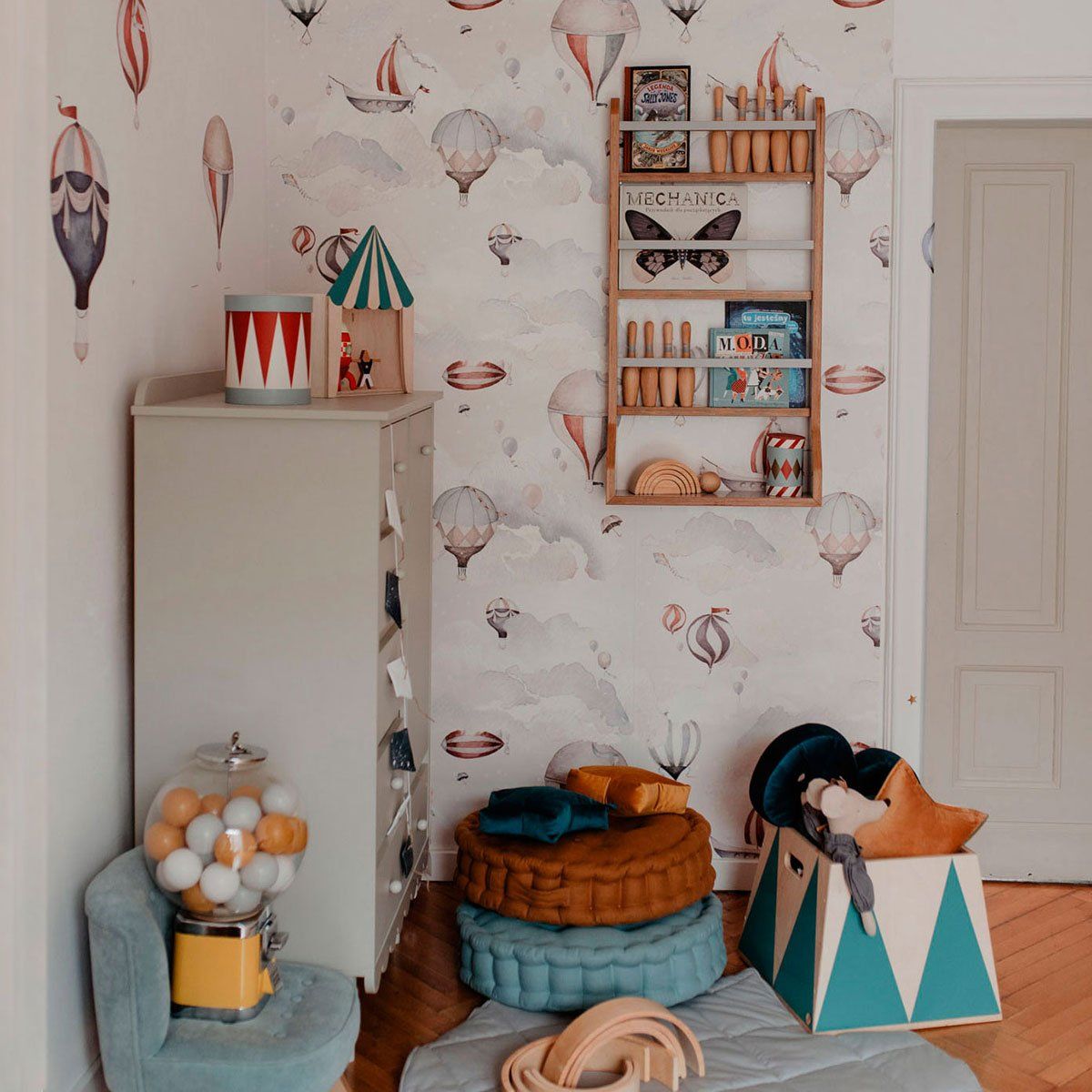 Dekornik Behang Balloons Adventure — Een avontuurlijk behang met kleurrijke luchtballonnen die over wolken en heuvels zweven, perfect voor een speelse, dromerige kinderkamer. Sfeerbeeld van het behang in een ingerichte kinderkamer.